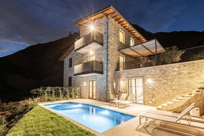 Una casa moderna de dos pisos con fachada de piedra, una piscina y una escalera que lleva a un balcón.
