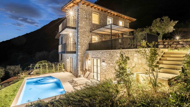 Ein zweistöckiges Steinhaus mit Swimmingpool, Sitzgelegenheiten im Freien und einer Treppe, die zu einem Balkon führt.