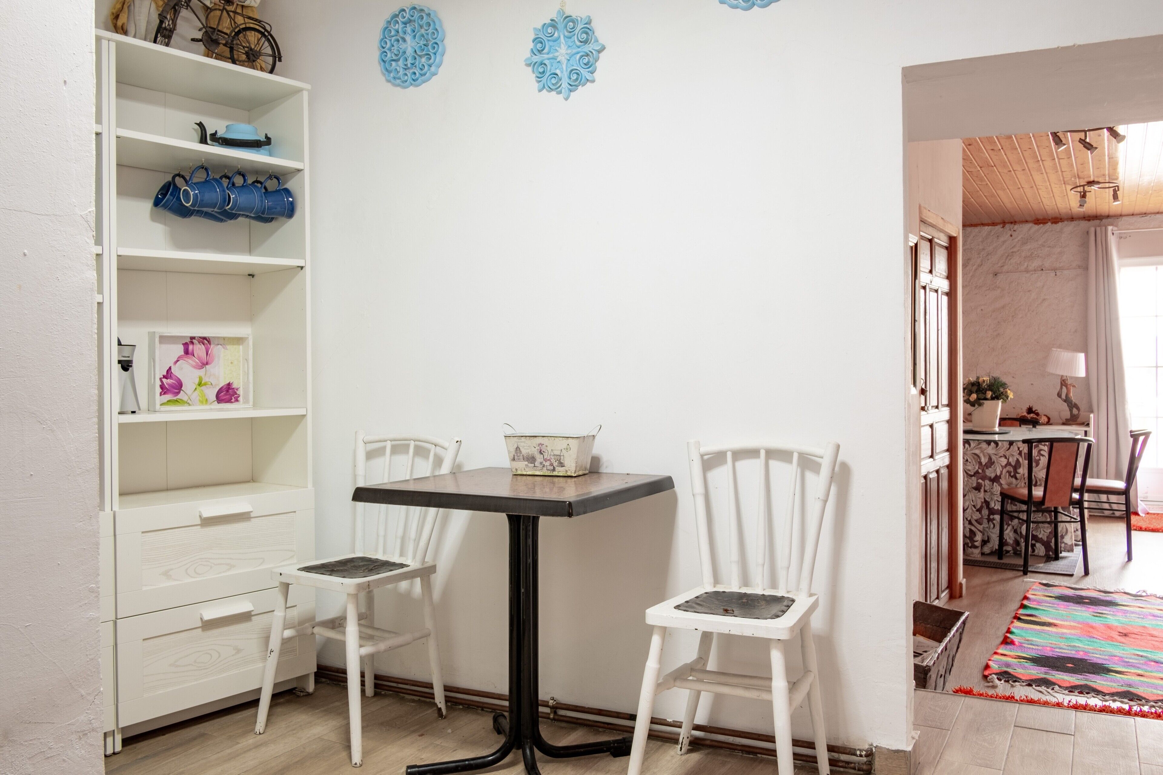 A room with a white cabinet, two chairs, a table, and a colorful rug.