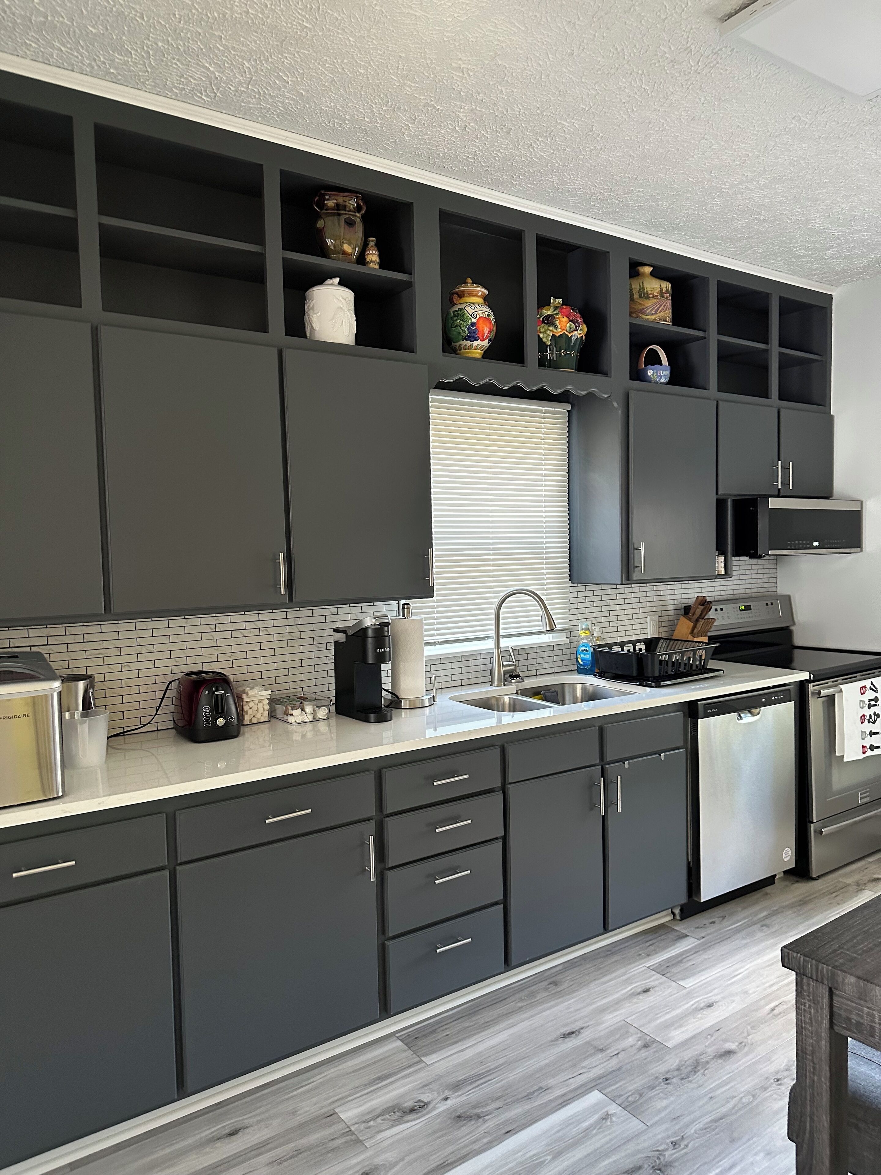 Eine moderne Küche mit dunklen Schränken, einem Edelstahl-Kühlschrank und einer gefliesten Spritzschutzwand.