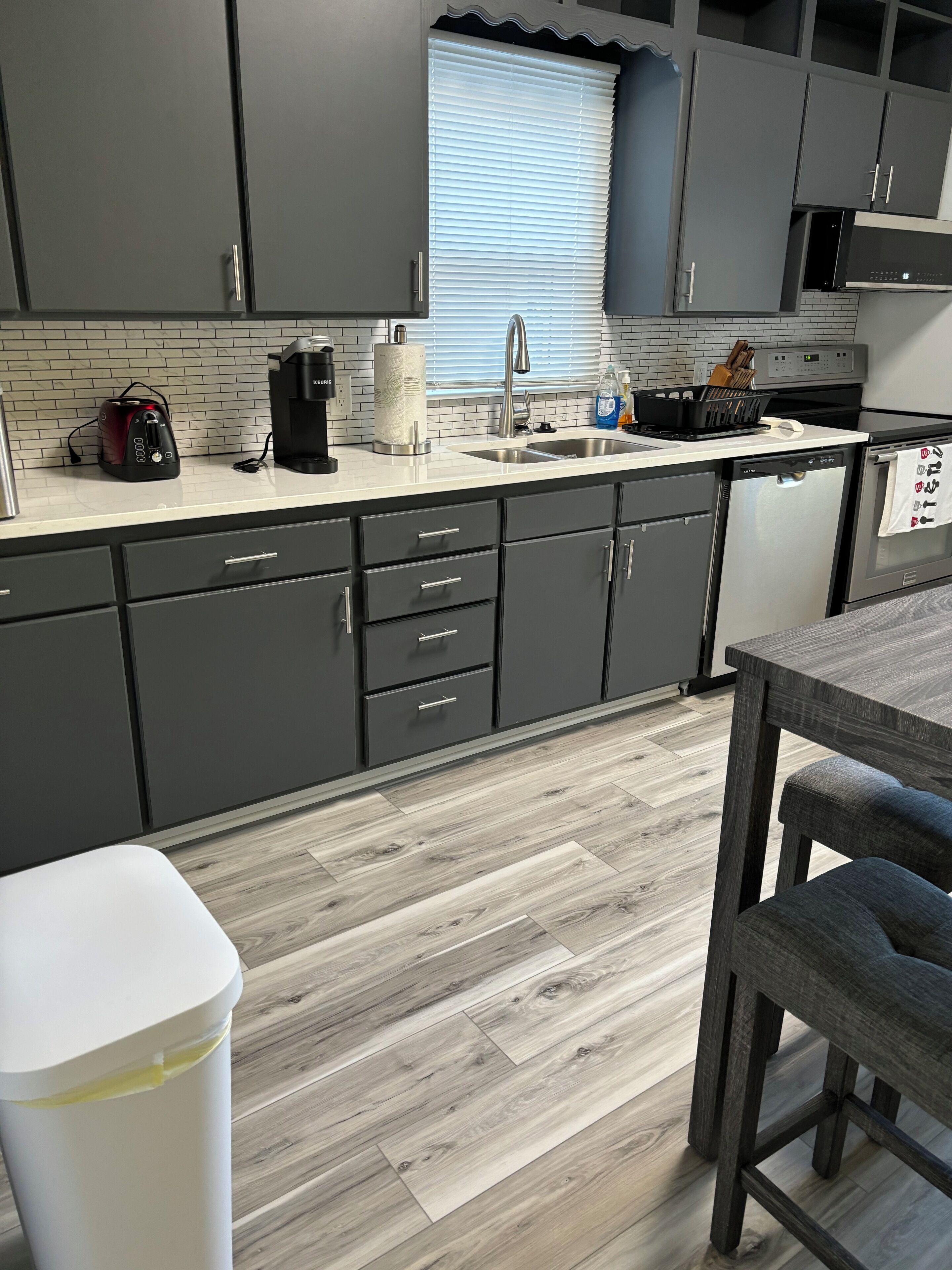 Una cocina moderna con armarios grises, encimera blanca y suelo de madera.