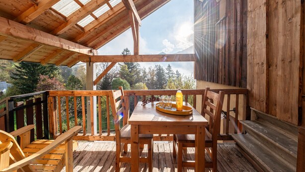 A wooden deck with a table and chairs, a bottle, and a tray. - Apartment 'Chalet La Vourze' with Private Terrace, Balcony and Wi-Fi (QUEIGE)