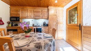 A wooden kitchen with a dining table set for two, a microwave, and a tiled backsplash. - Apartment 'Chalet La Vourze' with Private Terrace, Balcony and Wi-Fi (QUEIGE)