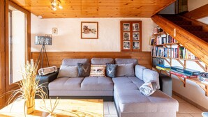 A cozy living room with a sectional sofa, a coffee table, a bookshelf, and a staircase. - Apartment 'Chalet La Vourze' with Private Terrace, Balcony and Wi-Fi (QUEIGE)
