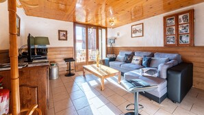 A wooden interior with a sofa, a coffee table, and a desk with a computer. - Apartment 'Chalet La Vourze' with Private Terrace, Balcony and Wi-Fi (QUEIGE)