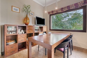 Un comedor con una mesa de madera, sillas, un televisor y una ventana con vistas a árboles.
