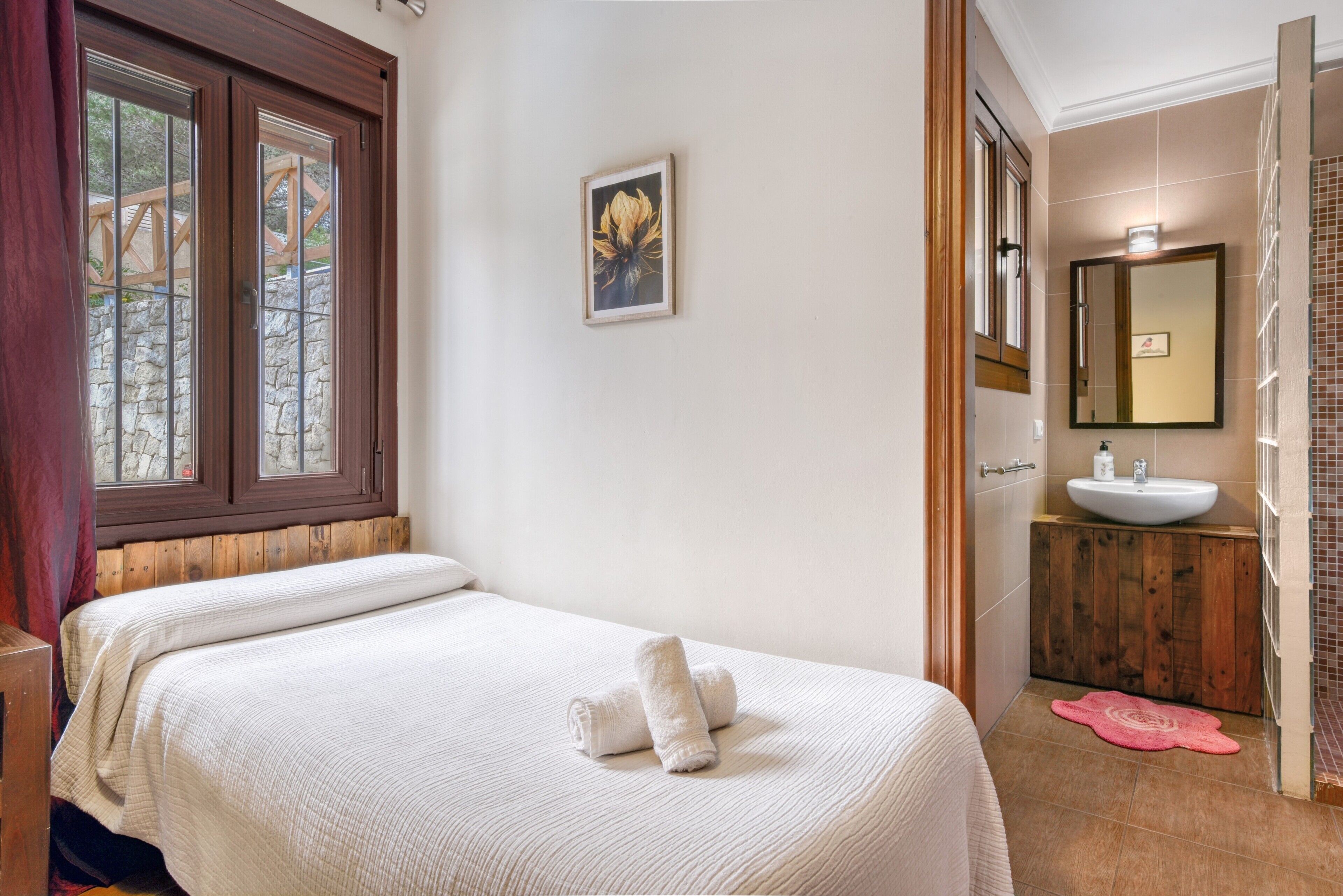 Hotelkamer met een bed, een schilderij, een badkamer met wastafel en spiegel, en een raam met uitzicht.