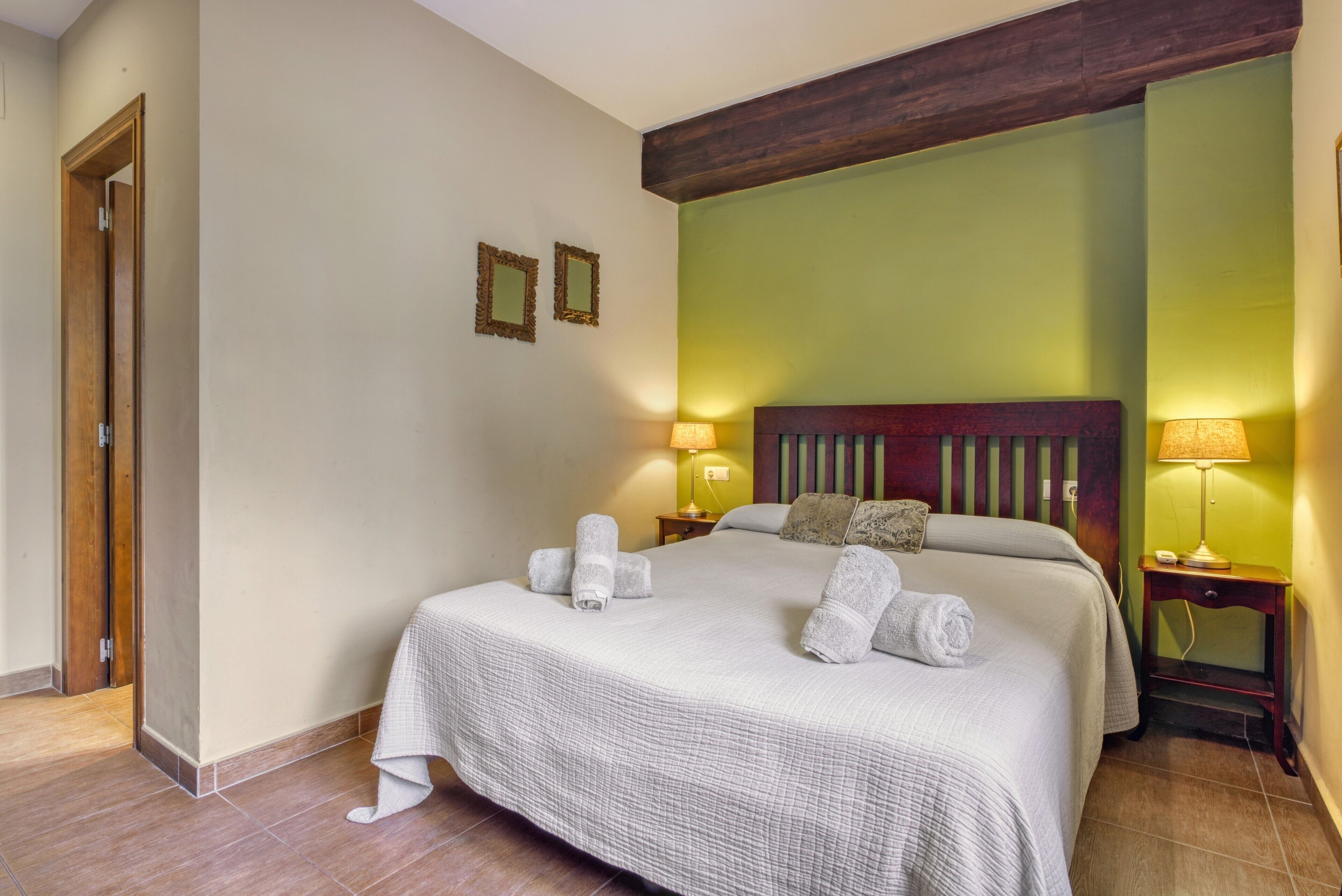 A hotel room with a bed, two bedside lamps, a wooden headboard, and a door.