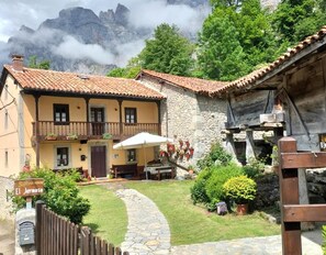 Un edificio de piedra tradicional con tejado de tejas, un camino de piedra y un pequeño jardín con plantas en macetas.
