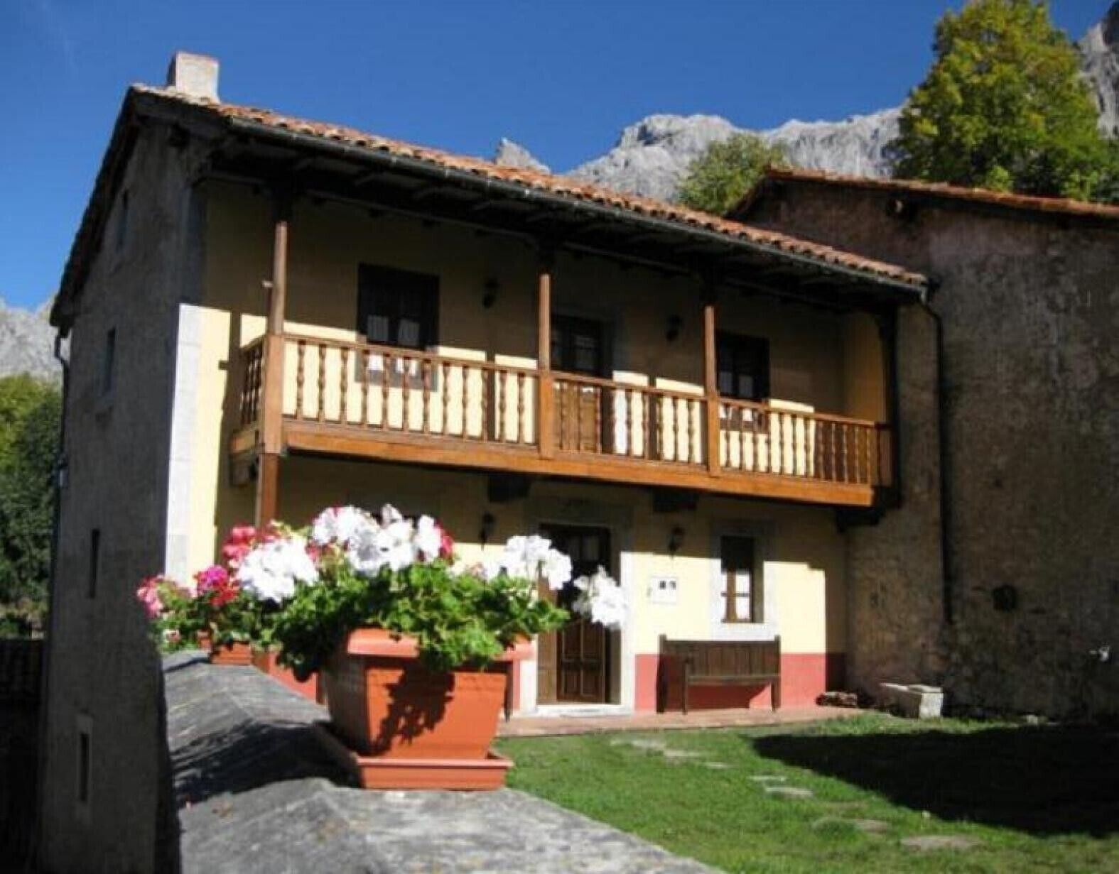 A two-story building with a balcony, a flower bed in front, and a mountain backdrop.