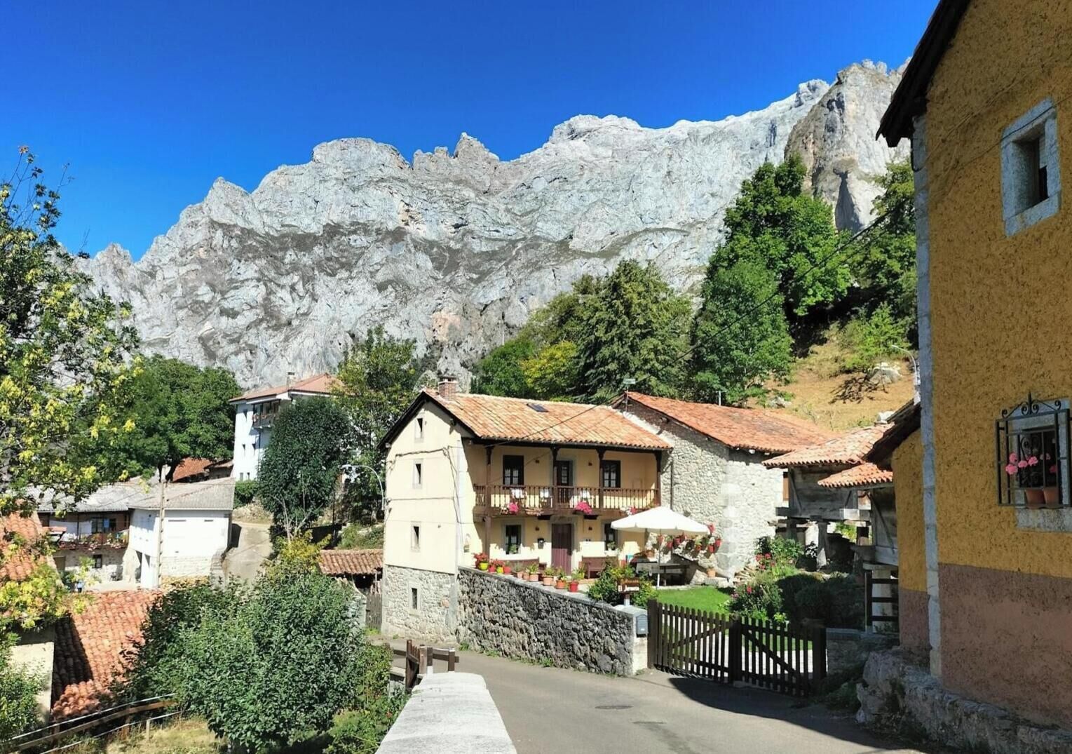 A mountain village with traditional stone buildings, a paved street, and a mountain backdrop.