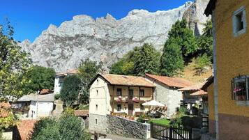 A mountain village with traditional stone buildings, a paved street, and a mountain backdrop.