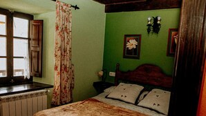 Un dormitorio con cama de madera, radiador, ventana con cortinas y pared verde.