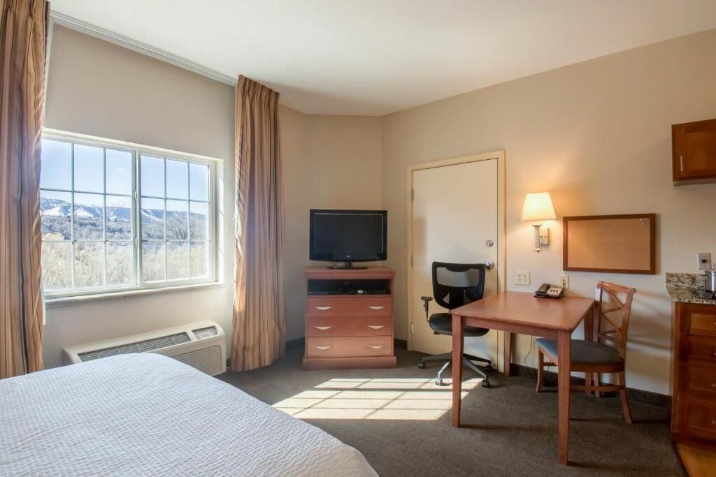 A hotel room with a bed, a desk, a chair, a television, and a window with curtains.