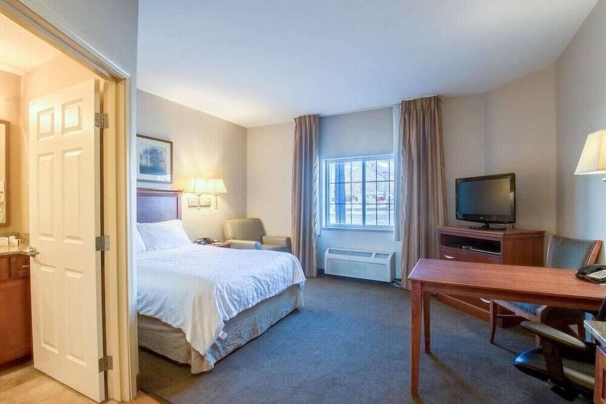 A hotel room with a bed, a desk, a television, and a window with curtains.