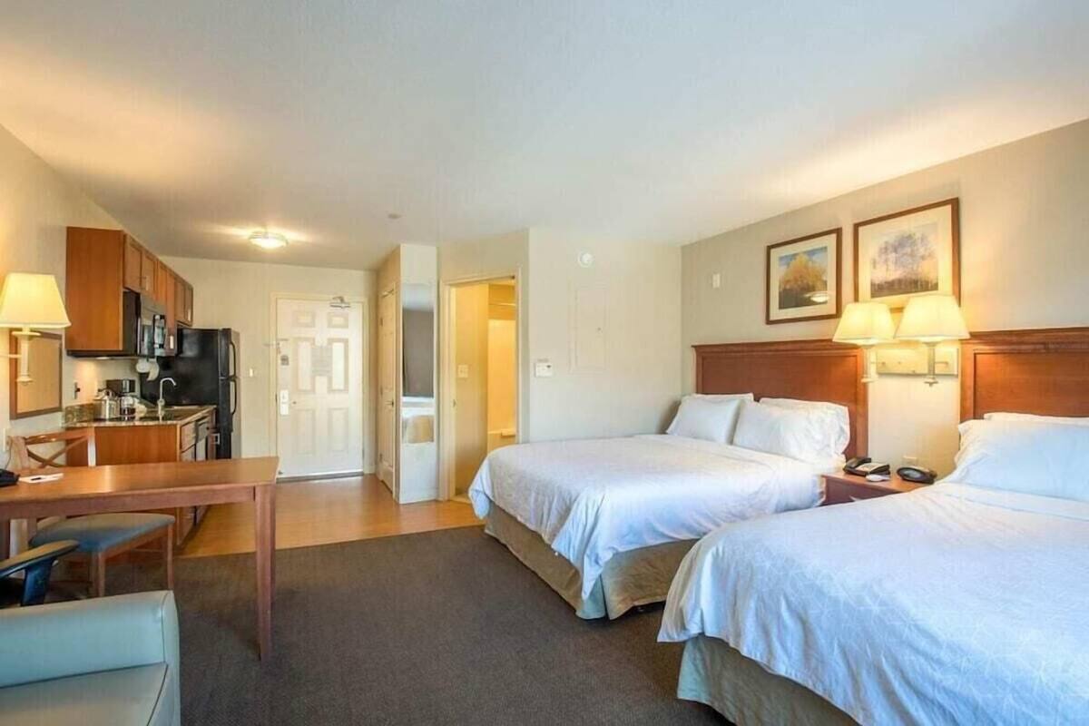 A hotel room with two beds, a kitchenette, a dining area, and a door leading to a bathroom.