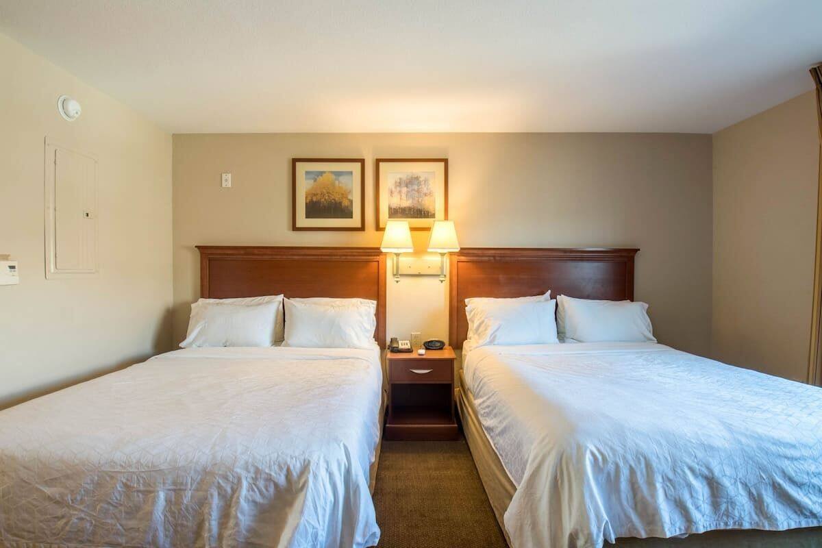 A hotel room with two single beds, a wooden headboard, bedside lamps, and two framed pictures on the wall.