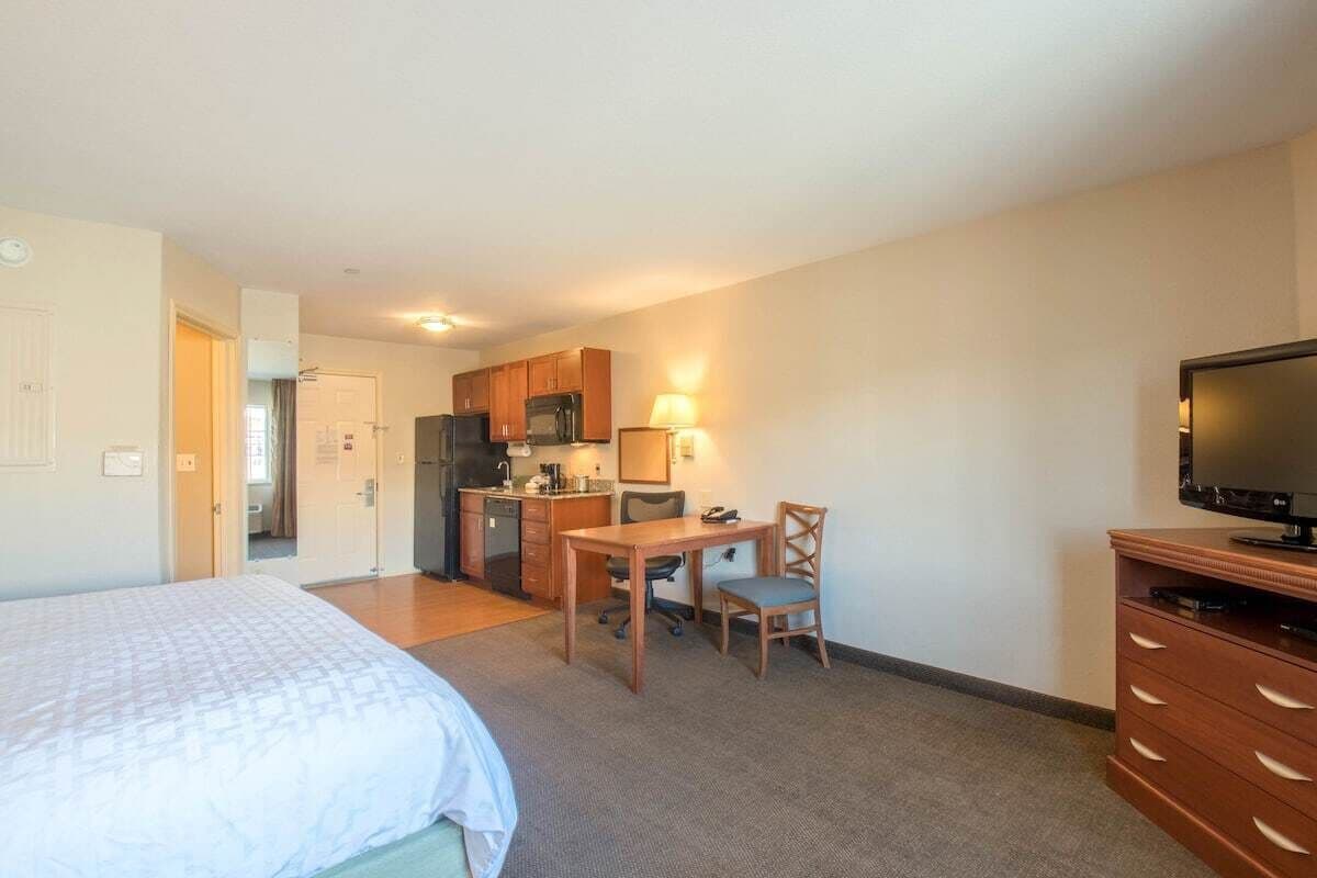 A hotel room with a bed, a desk with a chair, a television, a kitchenette, and a bathroom.