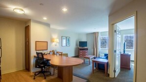 A hotel room with a wooden dining table, chairs, a TV, a desk, and a window with curtains. - Western Slope suites (Parachute)