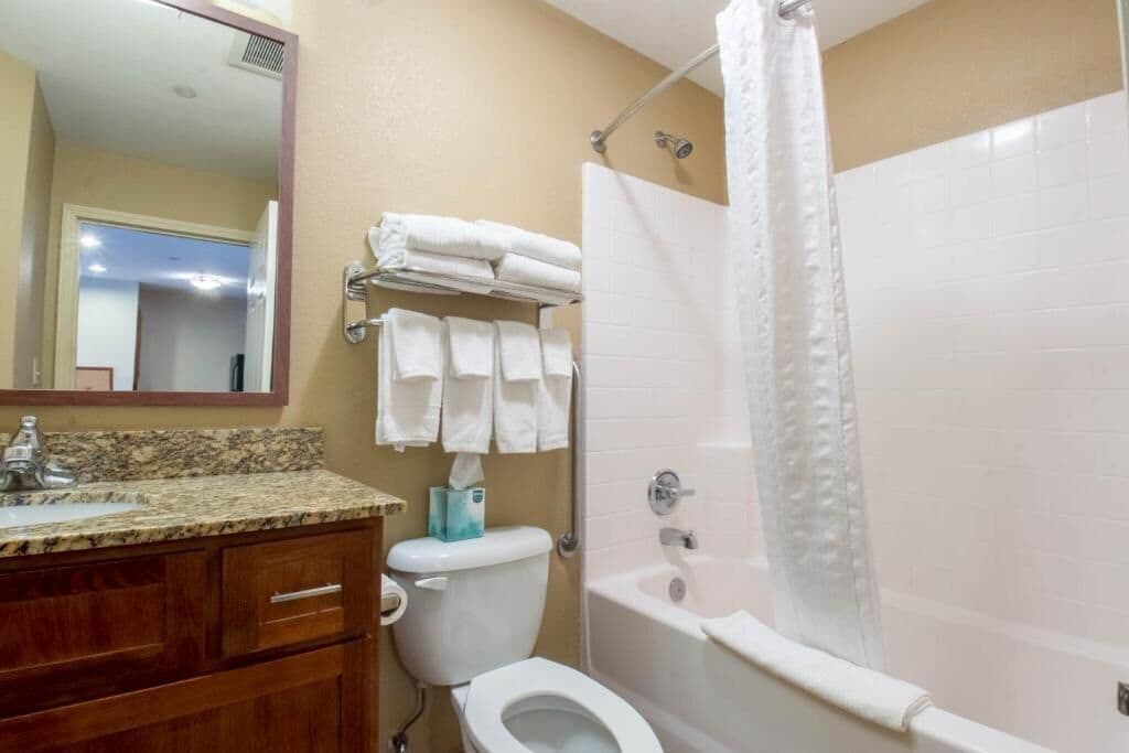 Un baño con inodoro, lavamanos y bañera. Hay toallas en un perchero y una cortina de ducha.