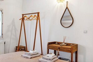 A room with a bed, a wooden table with a mirror, a wooden hanger stand, and a radiator.