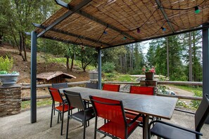An outdoor patio with a table and chairs, surrounded by stone walls and a view of a forested hillside.