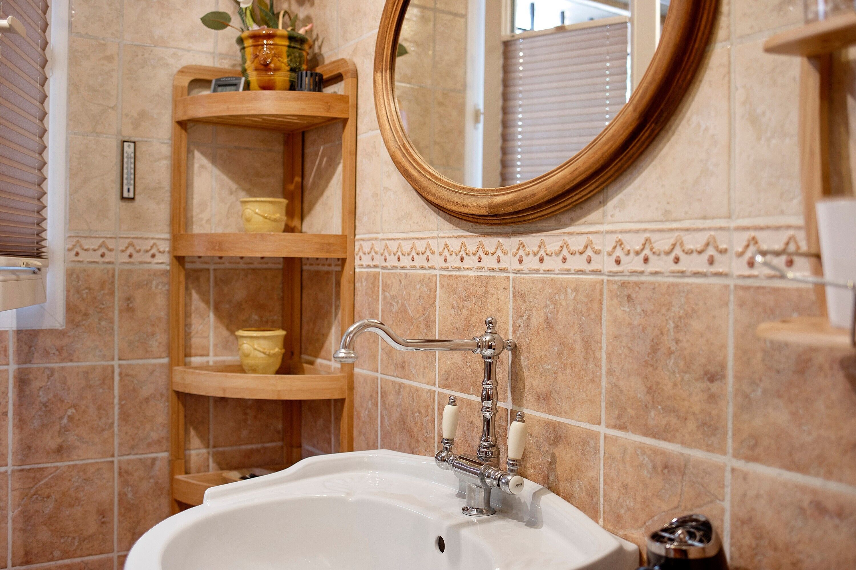 A bathroom with a white sink, wooden shelves, a mirror, and tiled walls.