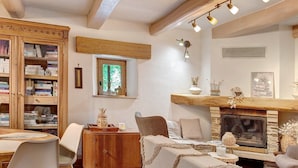 A cozy living room with a fireplace, a wooden cabinet with books, a dining table with chairs, and a window with natural light. - Ground Floor Room 'Le Mont Aigoual' 15 m² (Saumane)