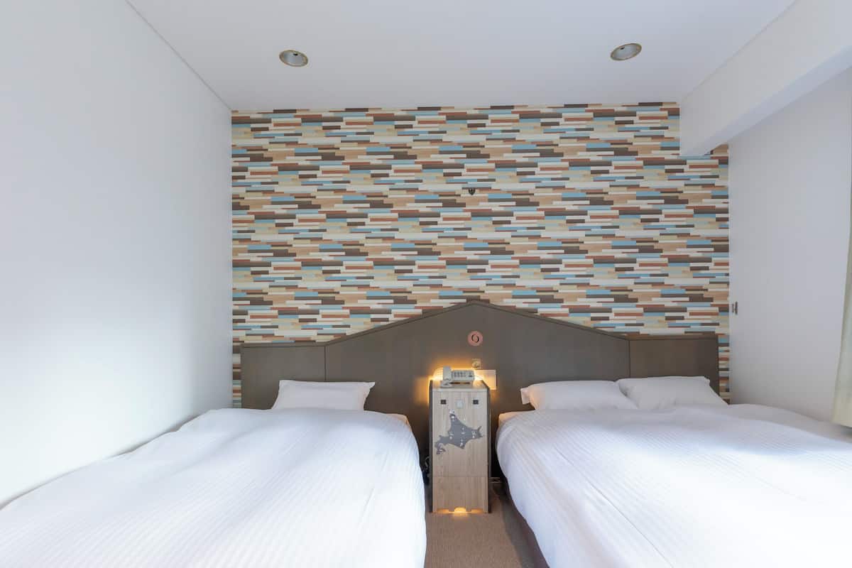 Two single beds with white linens, a geometric-patterned headboard, and a wall clock create a stylish space.