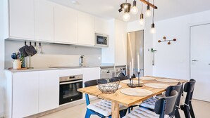 A modern kitchen with white cabinets, a microwave, a stove, and a dining area with a wooden table and chairs. - Apartment 'Bc01 El Sueño Marinsa Beach 2' with Sea View, Wi-Fi and Air Conditioning (El Morche)