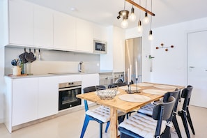 Una cocina moderna con armarios blancos, microondas, estufa y comedor con mesa y sillas de madera.
