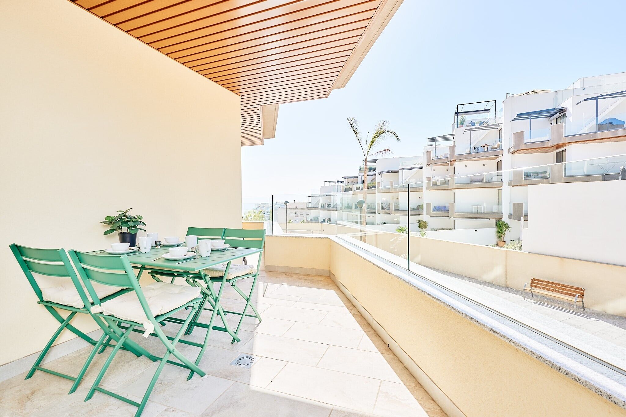 A balcony with a table and chairs, a potted plant, and a view of adjacent buildings.