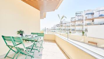 A balcony with a table and chairs, a potted plant, and a view of adjacent buildings.