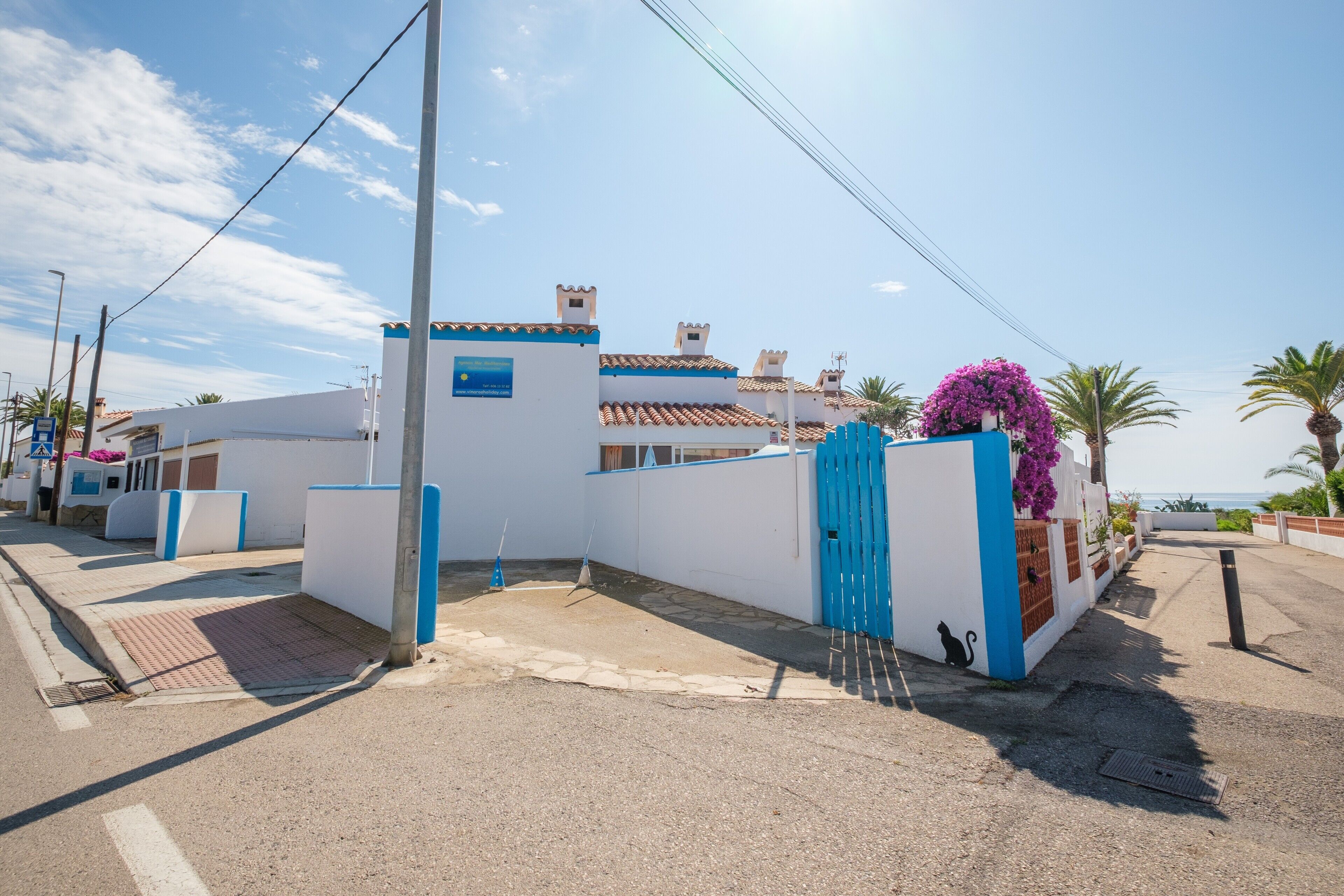 Une propriété située sur la côte, dotée d’une entrée sécurisée par un portail, d’une façade bleue et blanche et offrant une vue sur la mer.