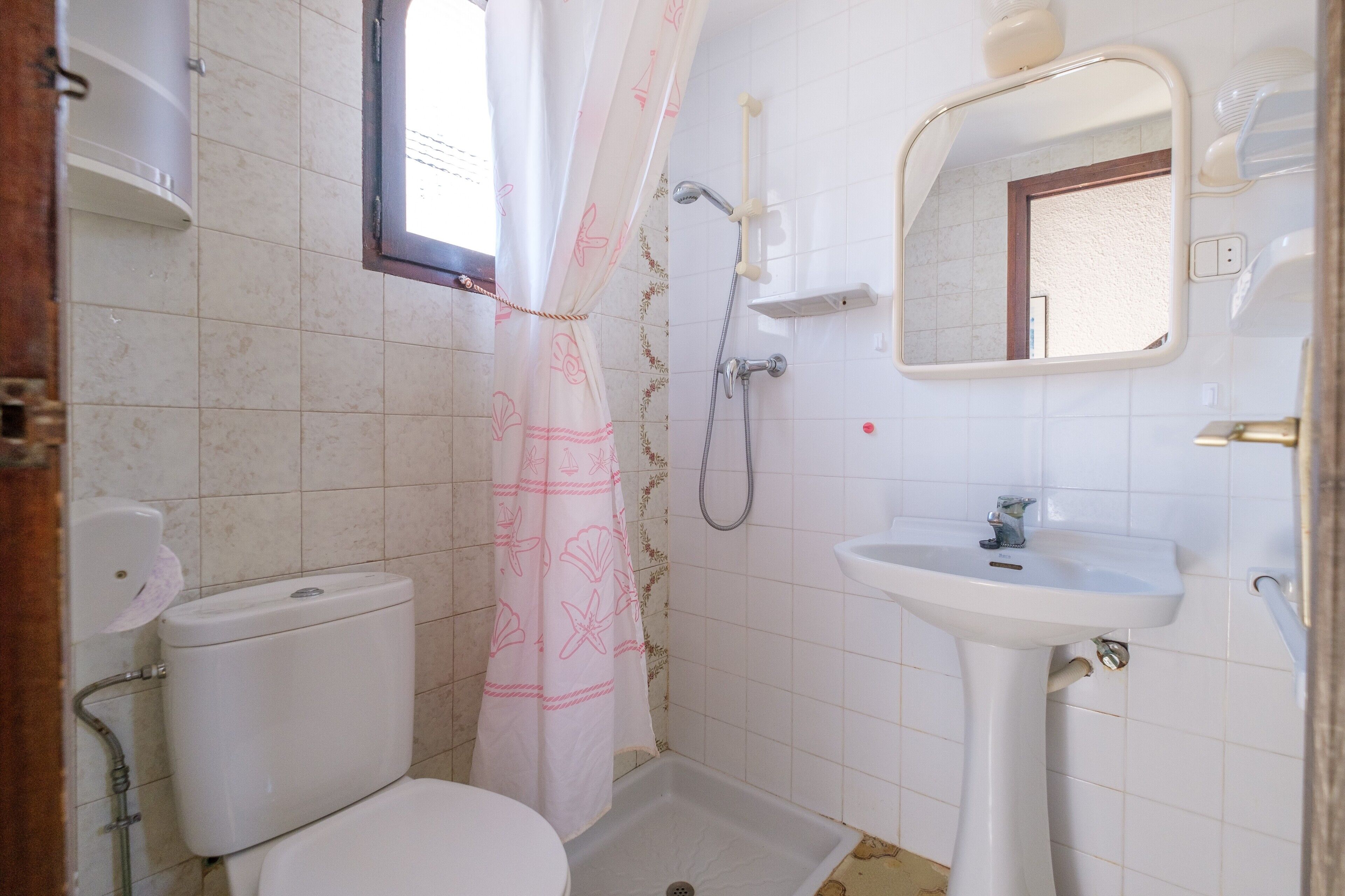Ein Badezimmer mit Toilette, Dusche, Waschbecken und einem Fenster mit Vorhang.