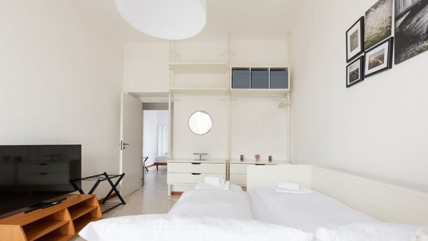 A modern hotel room with a TV, a bed, a wardrobe, and a round mirror. - GuestHost - Gambara M1 White Functional Appt x4 (Milano)