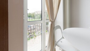 A room with a white table and chair, a window with curtains, and a view of a fenced outdoor area. - GuestHost - Gambara M1 White Functional Appt x4 (Milano)