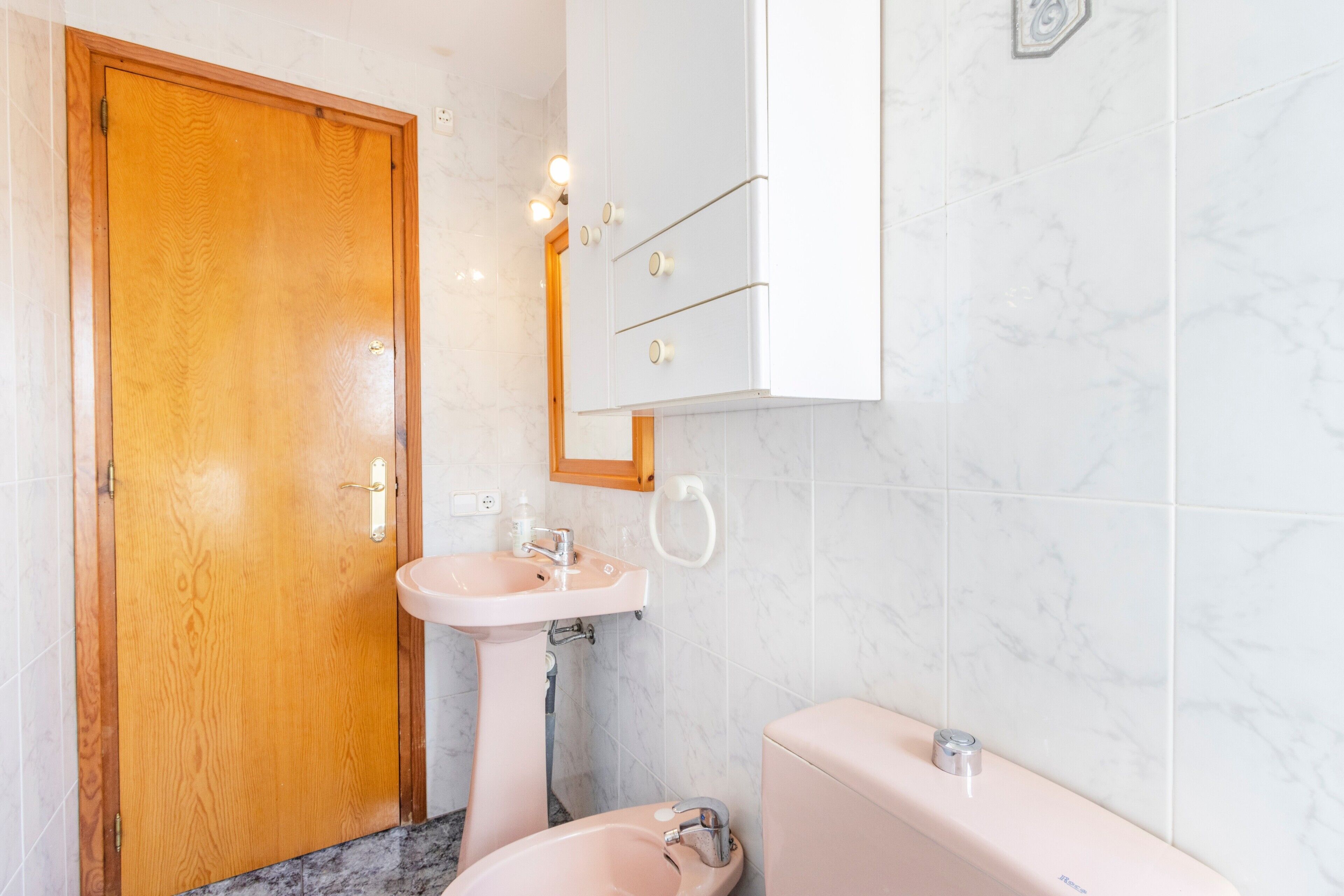 Un baño con puerta de madera, lavamanos, inodoro y espejo.