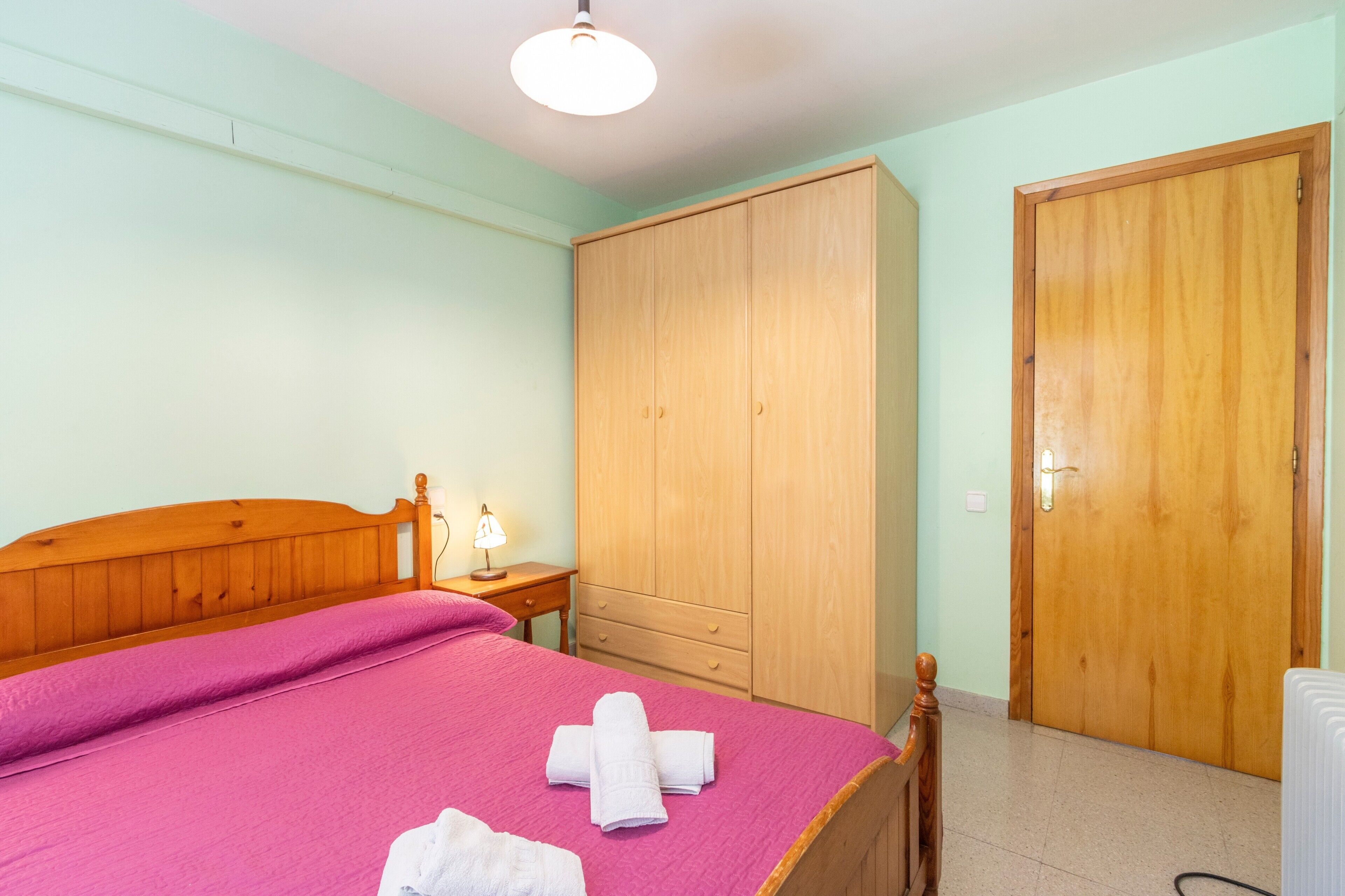 Un dormitorio con una cama de madera, un armario, una puerta y una mesita de noche con una lámpara.