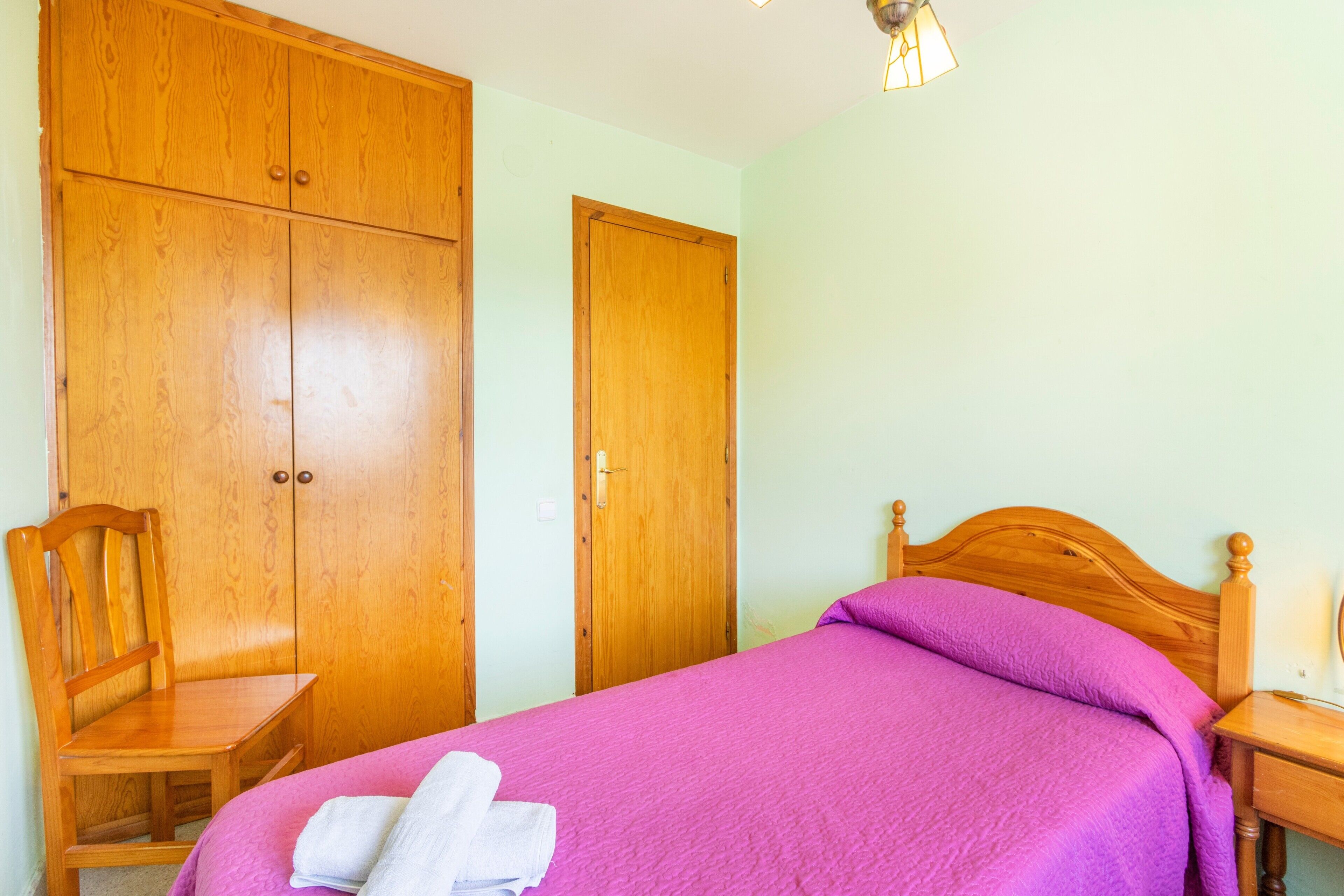 Un dormitorio con cama, armario de madera y una silla.