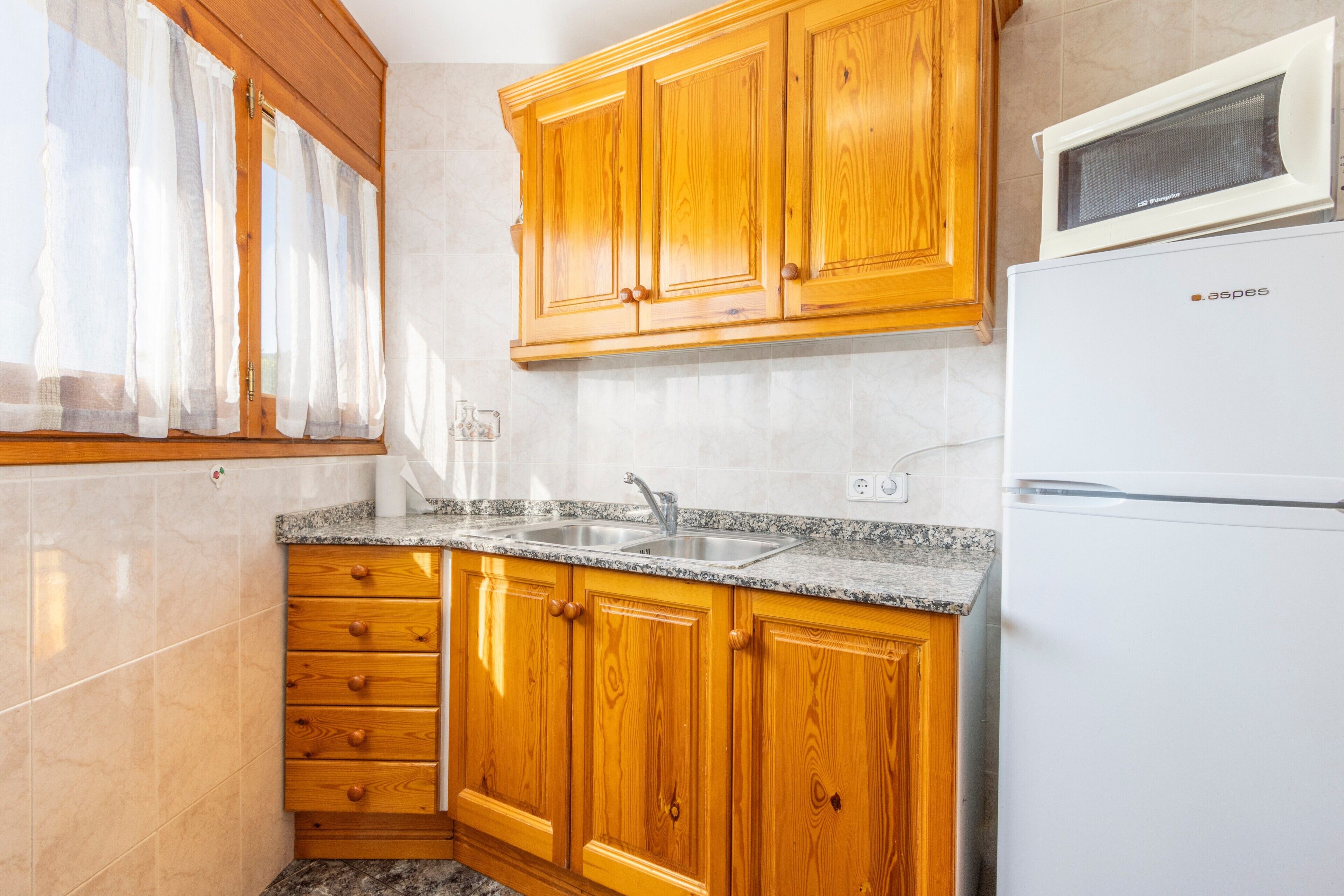 Una cocina con gabinetes de madera, encimera de granito, microondas integrado y pileta de acero inoxidable.
