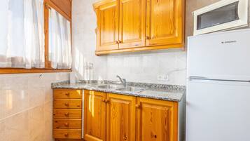 Una cocina con gabinetes de madera, encimera de granito, microondas integrado y pileta de acero inoxidable.