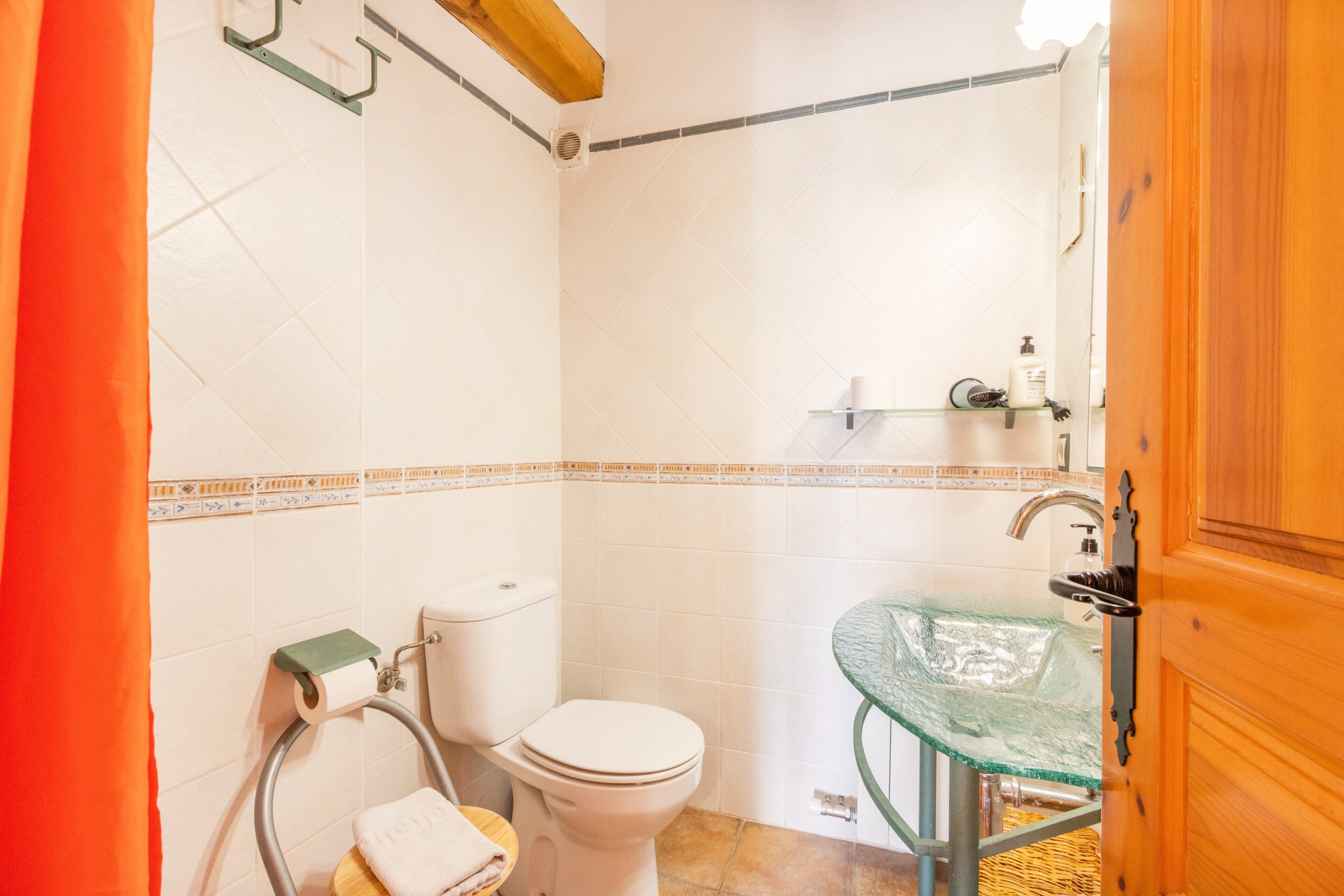 Une salle de bain avec des toilettes, un lavabo en verre, une douche et une porte en bois.