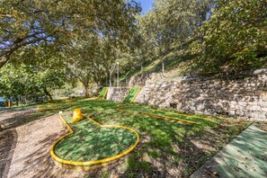 Un parc avec un sentier sinueux, un mur de pierre et une zone herbeuse parsemée d’arbres.