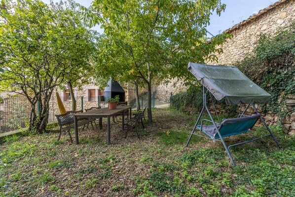 Un patio con una mesa y sillas, una zona de estar cubierta y un muro de piedra.