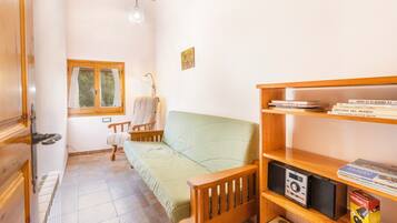 Una habitación acogedora con un banco de madera, un sofá verde, una mesita con una lámpara, una ventana con cortinas y una estantería con libros y una cámara.