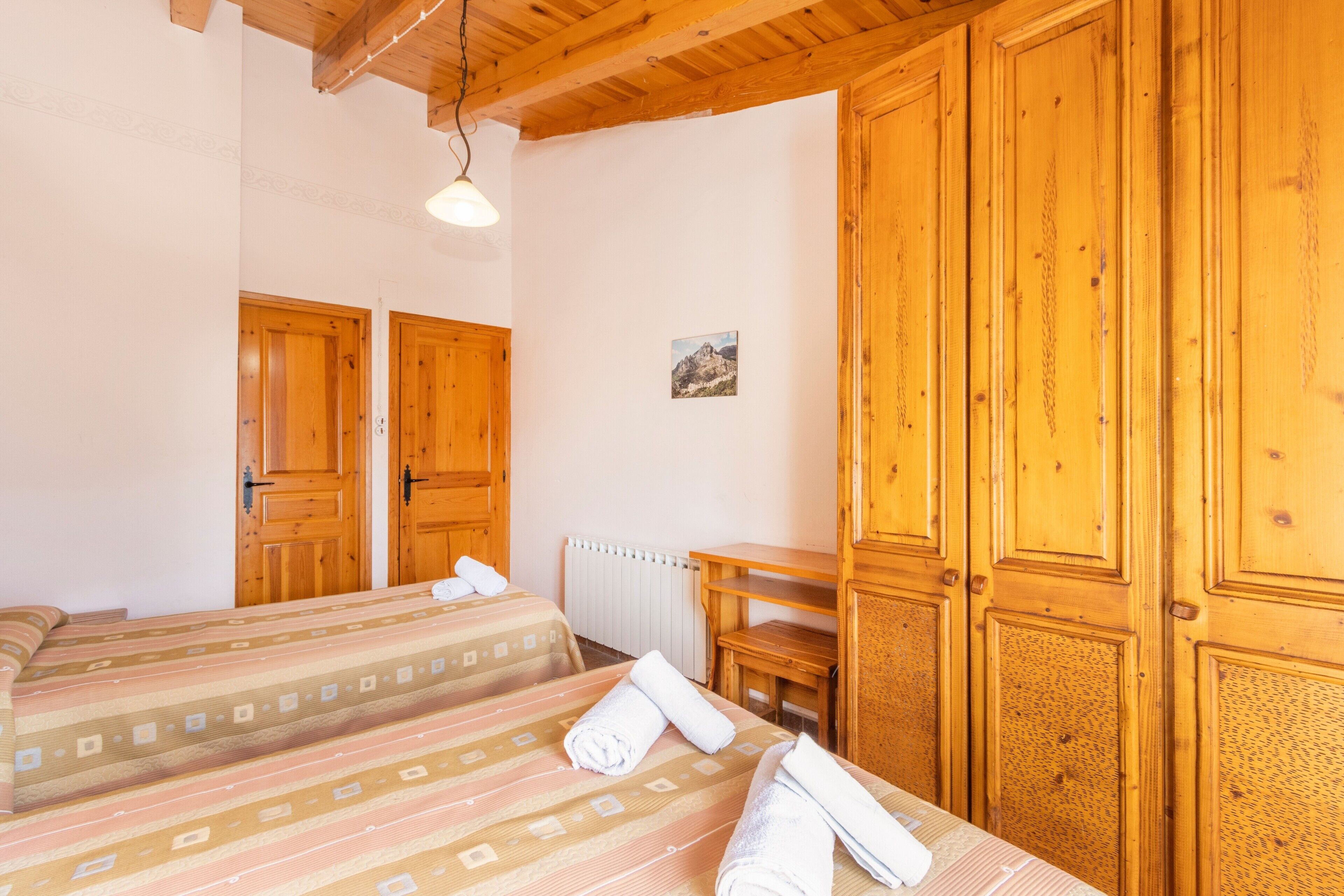 Quarto com duas camas, guarda-roupa de madeira, uma mesinha e radiador.