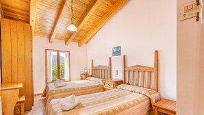 A room with two beds, wooden headboards, a desk, and a window with curtains.
