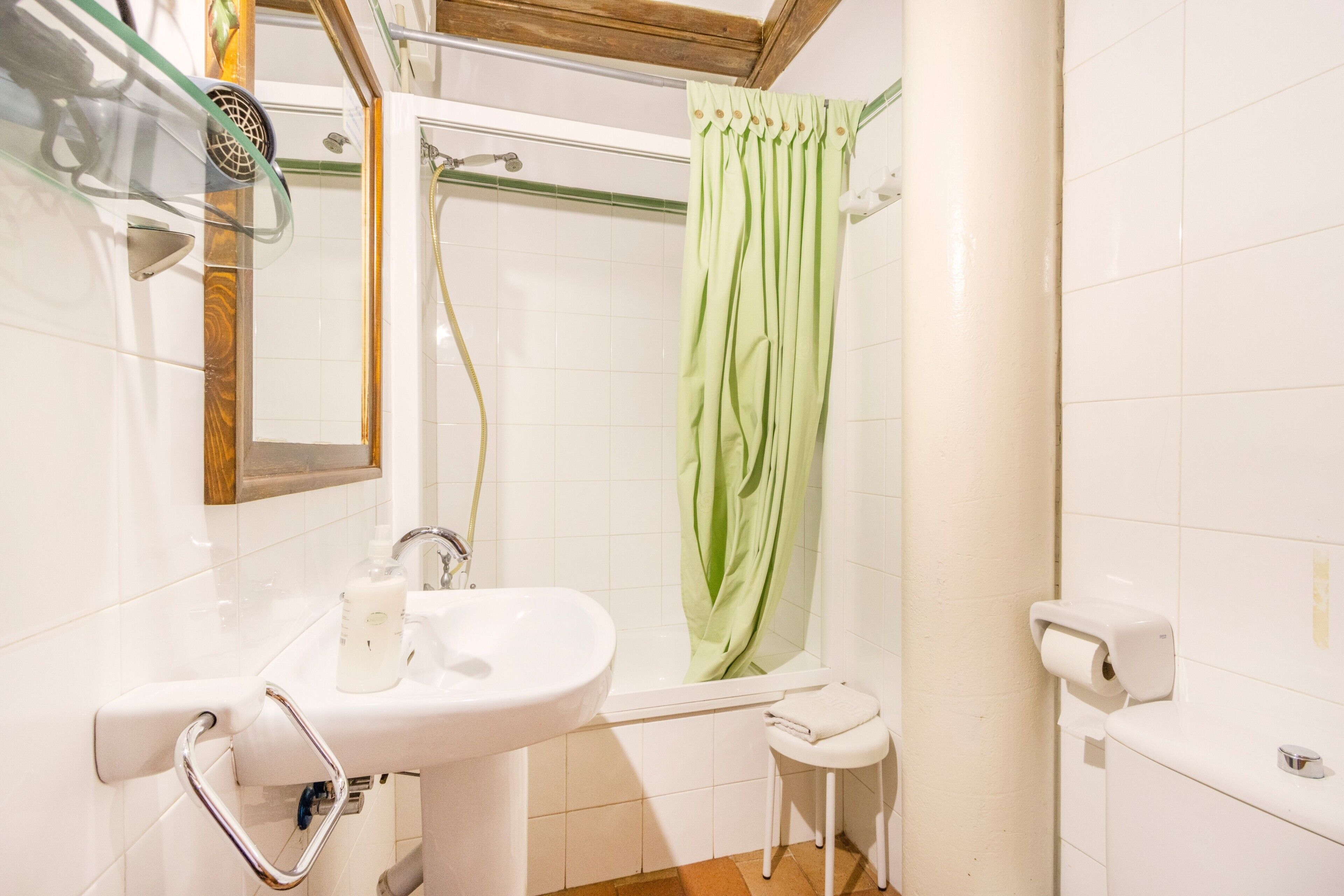 Un baño con lavabo, espejo, ducha y dispensador de papel higiénico.