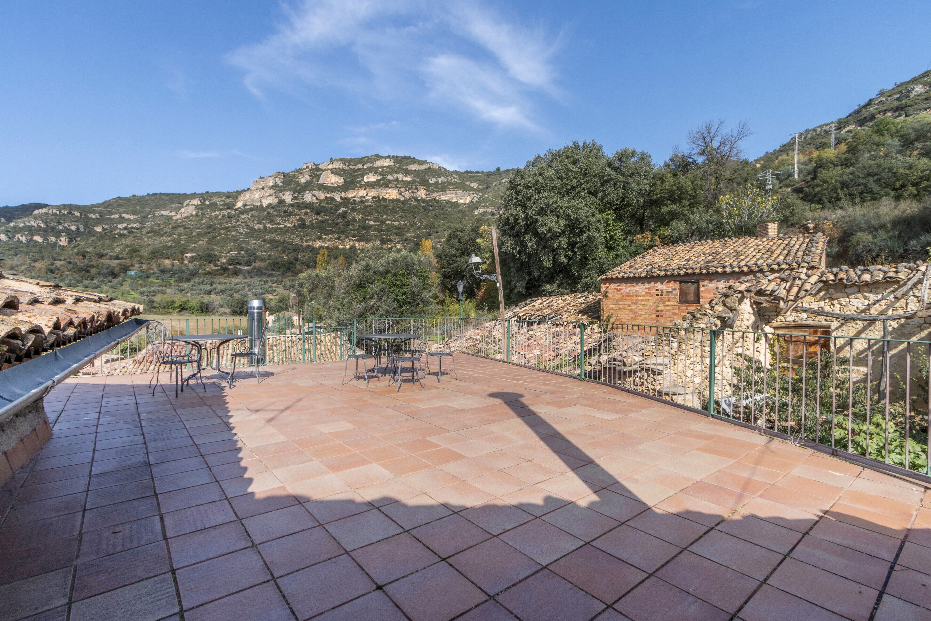 Eine Terrasse mit Tisch und Stühlen, ein kleines Backsteinhaus und eine gebirgige Kulisse.